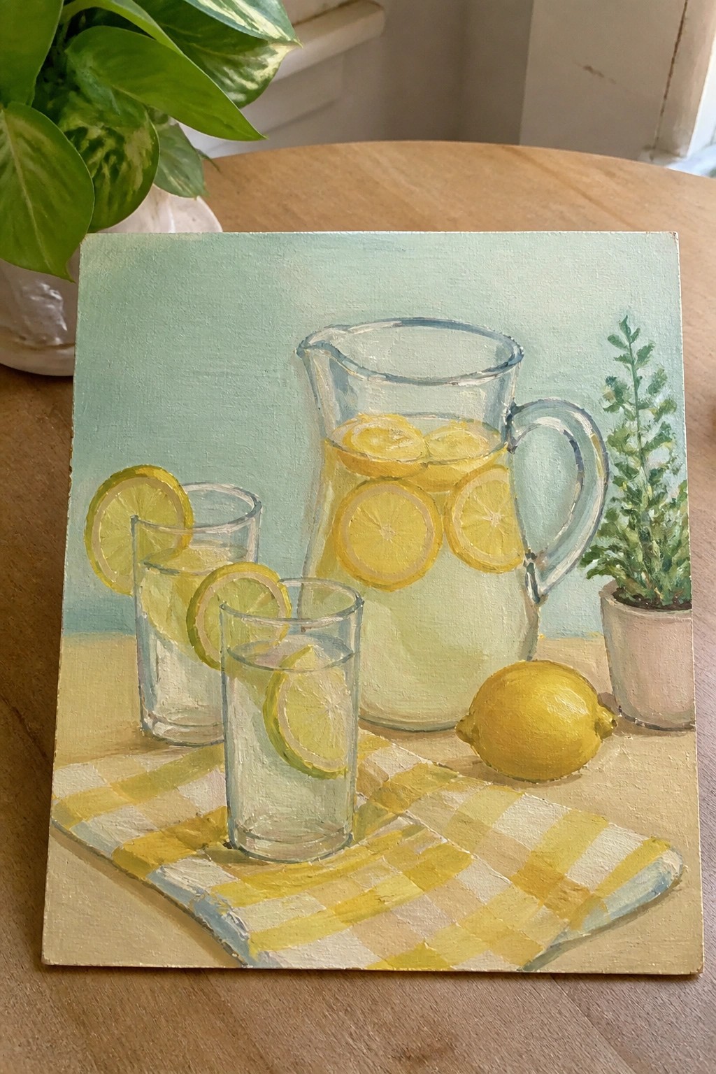 Still-life painting of lemonade pitcher, glasses with lemon slices, and checkered cloth.