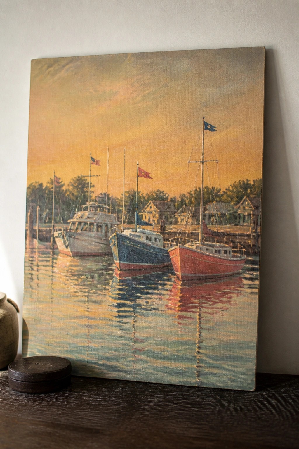 Realistic painting of red, blue, and white boats docked at sunset with reflections.