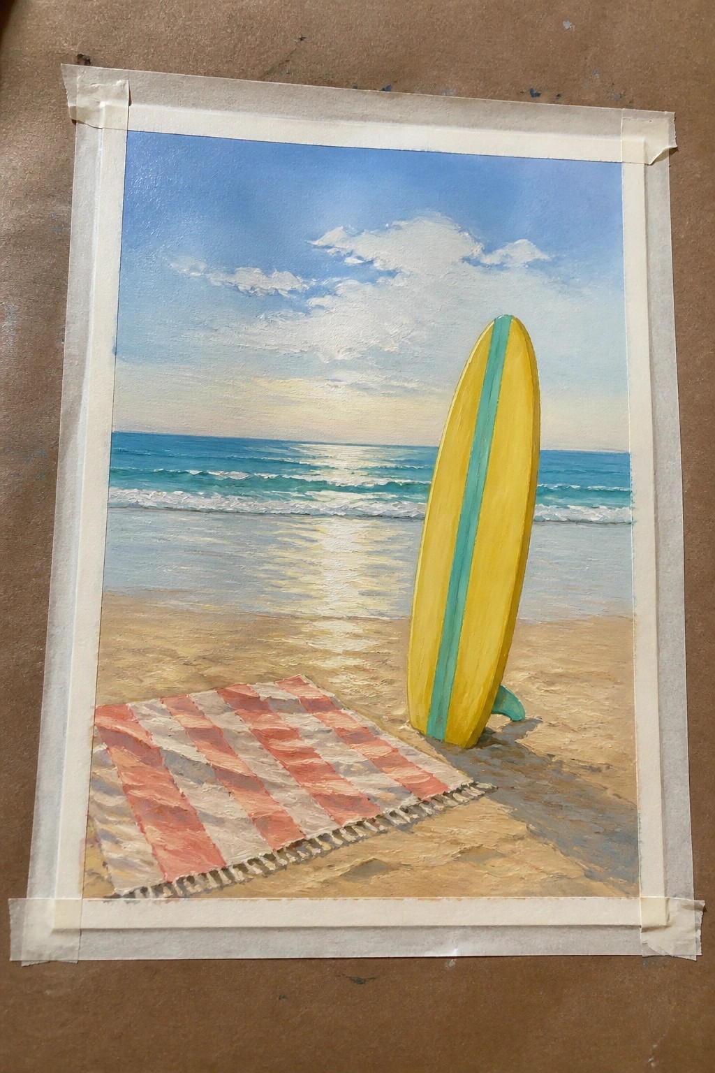 Yellow surfboard with teal stripe beside striped towel on sunny beach by ocean