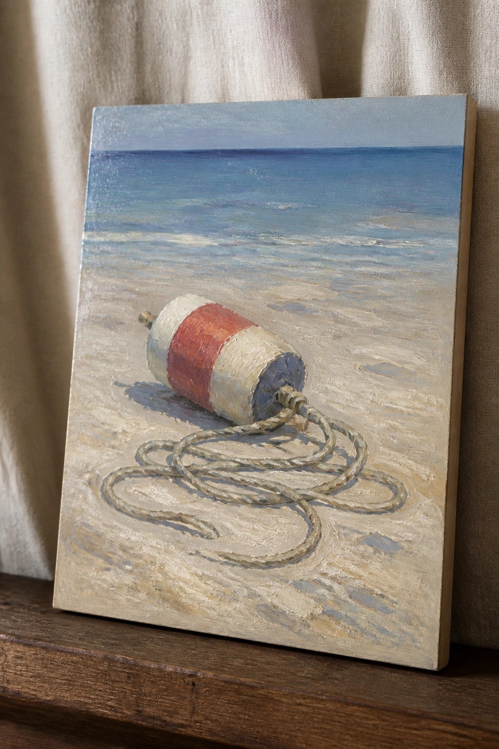 Painting of red and white buoy with coiled rope on sandy beach by ocean.