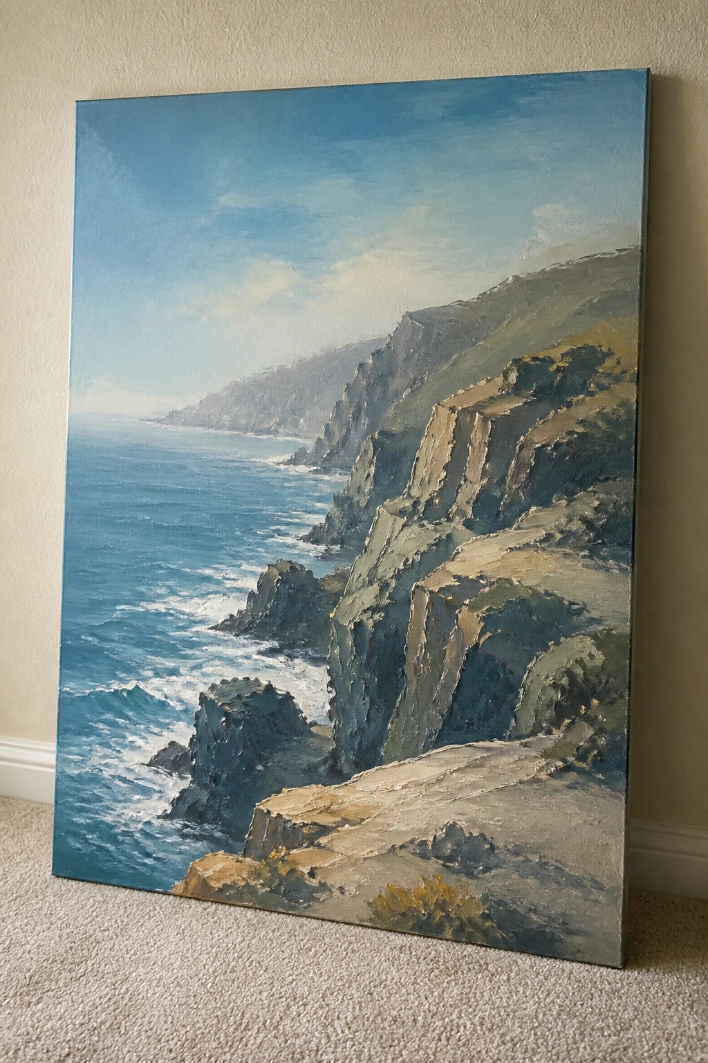 Oil painting of rugged cliffs overlooking blue ocean with waves, leaning on wall