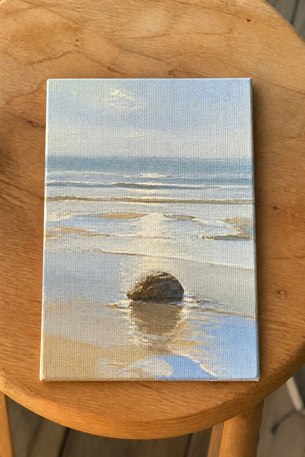 Miniature seascape painting of ocean waves and rock on wooden stool