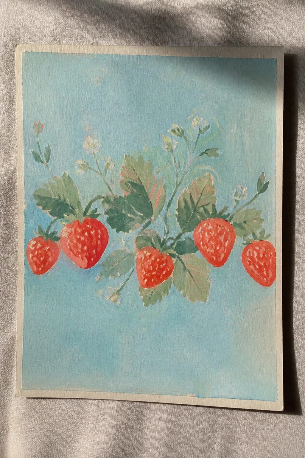 Watercolor painting of red strawberries with green leaves and white flowers on blue background.