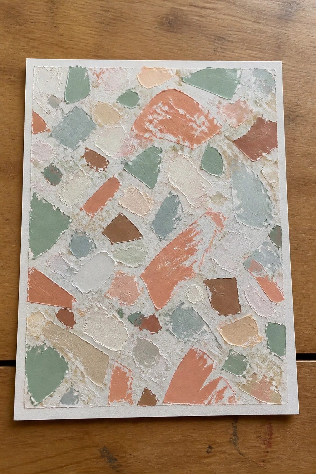 Abstract painting with irregular pastel shapes in coral, green, and beige on white canvas over wood.