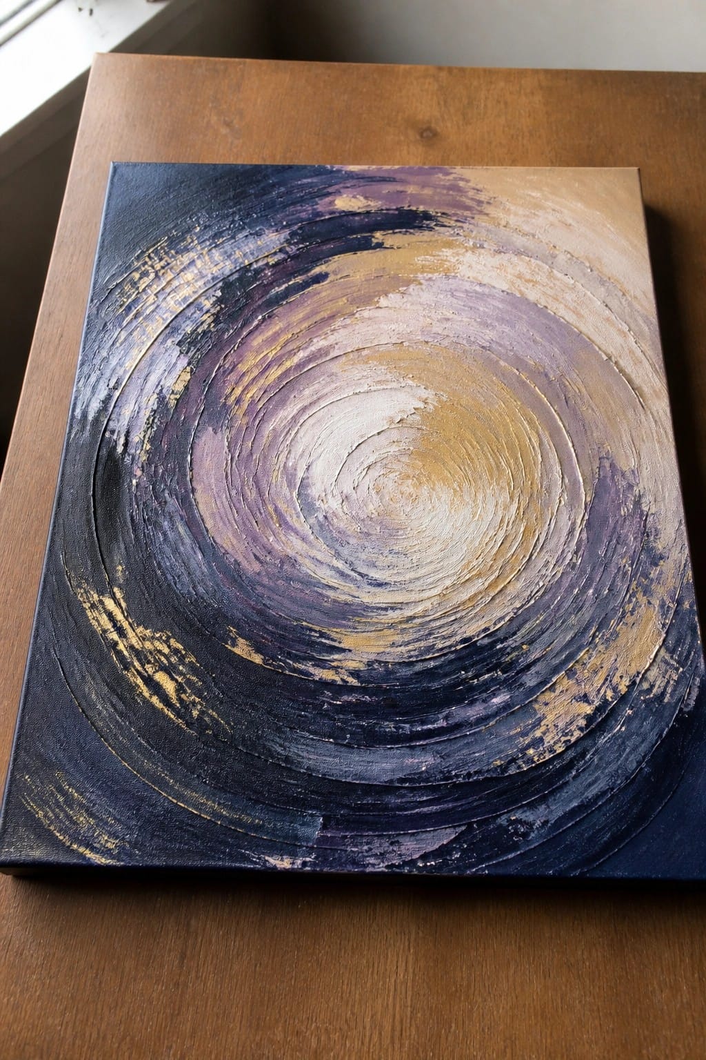 An abstract oil painting with thick swirling brushstrokes in dark blue, purple, gold, and white forming concentric circles on a canvas.