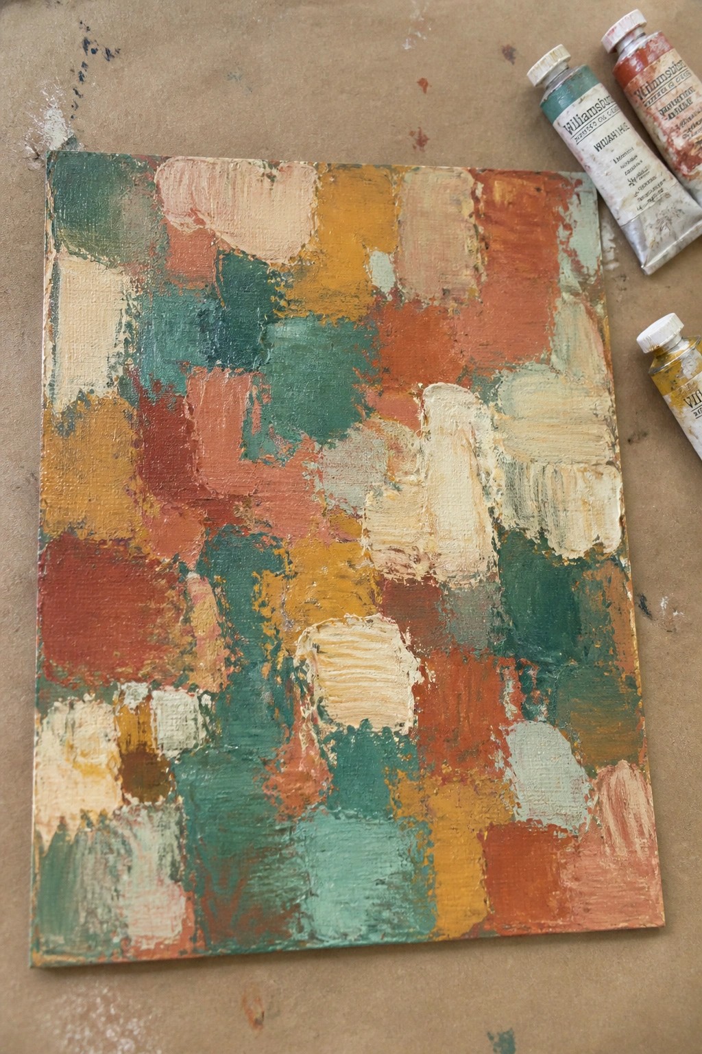 Abstract painting with thick green, orange and red brushstrokes beside oil paint tubes