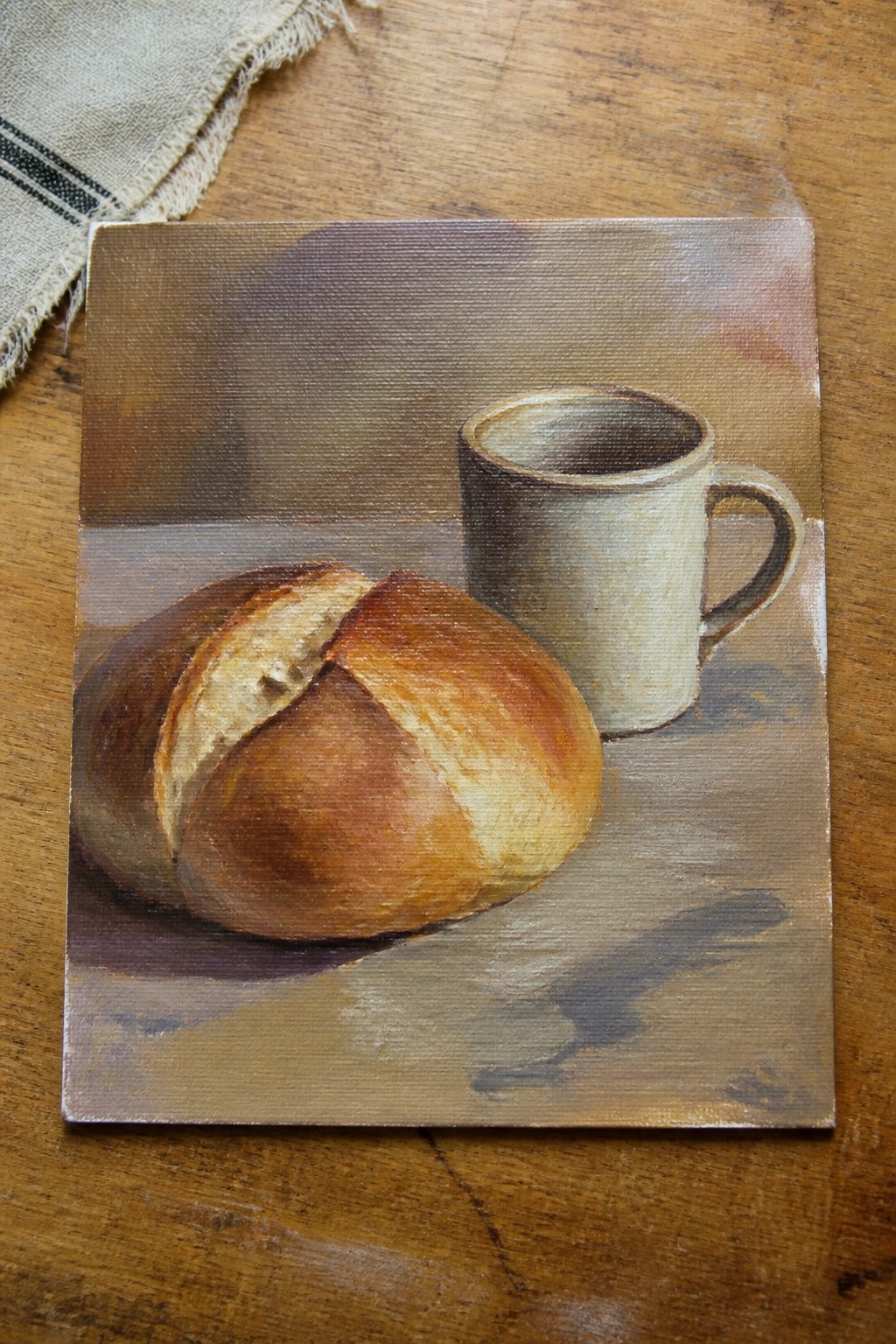 Realistic still life painting of crusty bread loaf and ceramic mug on wood.