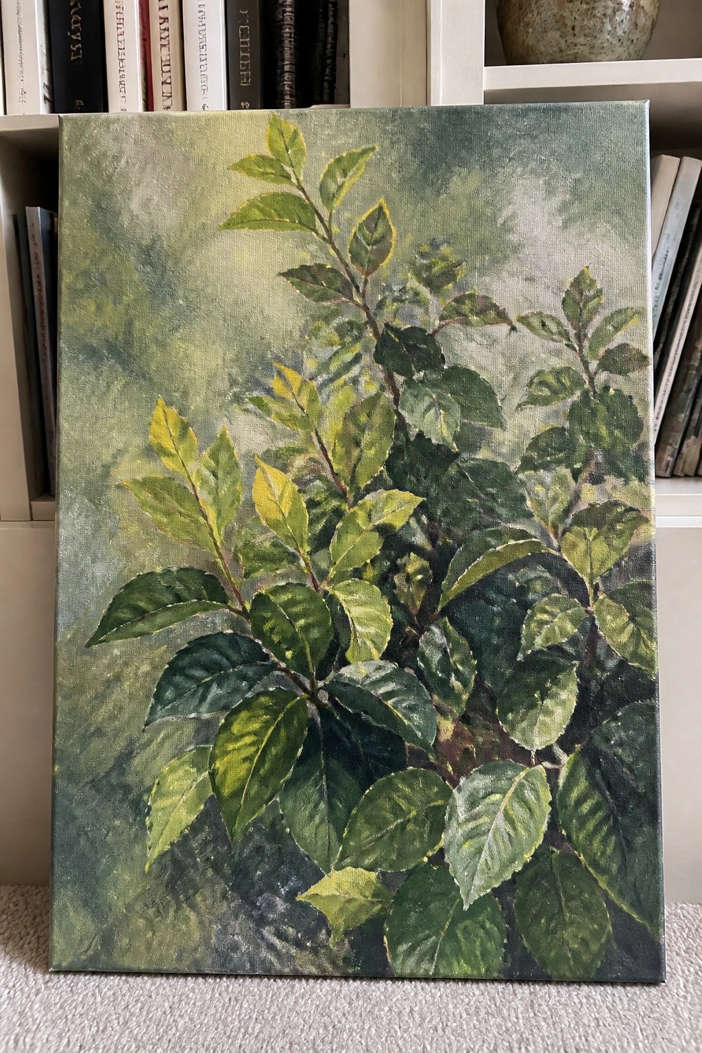 Leafy green plant painting with yellow accents leaning against a bookshelf.