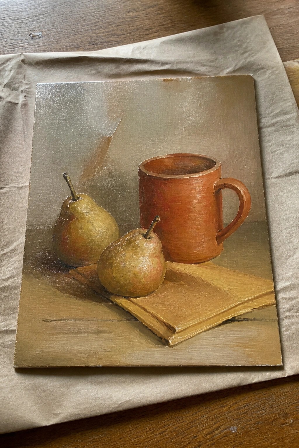 Realistic still life painting of two pears beside a brown mug on a book.