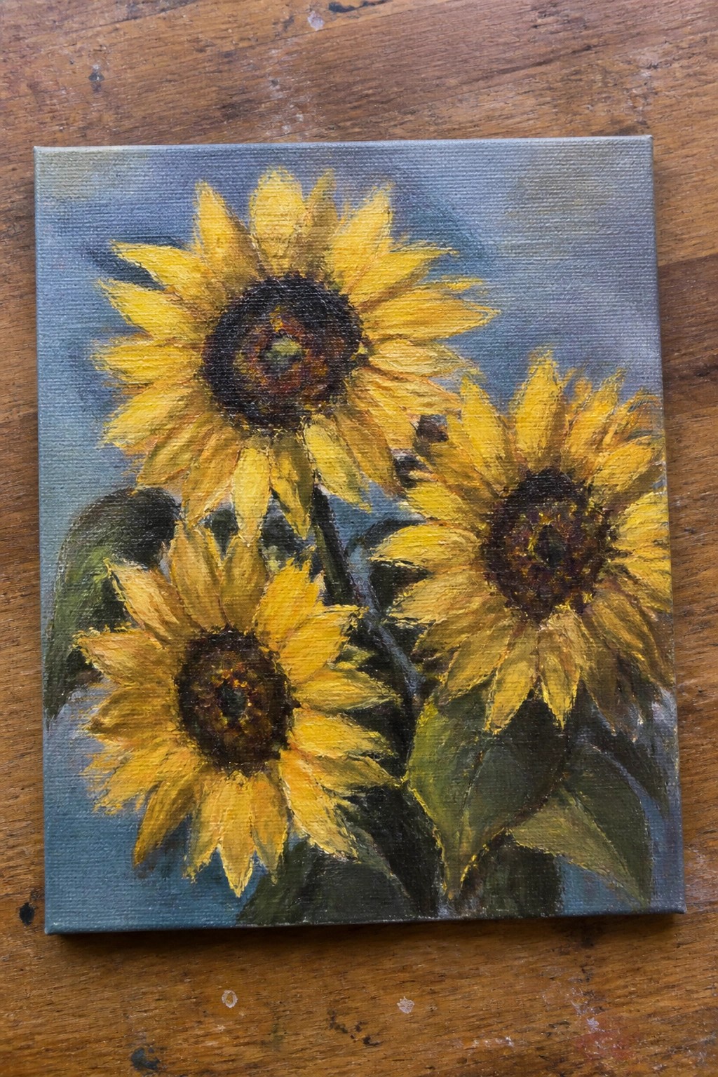 Vibrant oil painting of three yellow sunflowers with green leaves on canvas