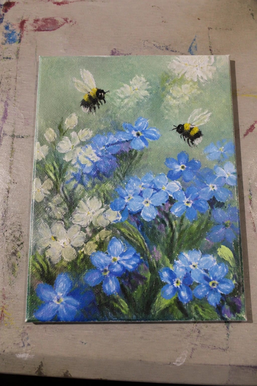 Oil painting on canvas showing blue and white flowers with two bumblebees.