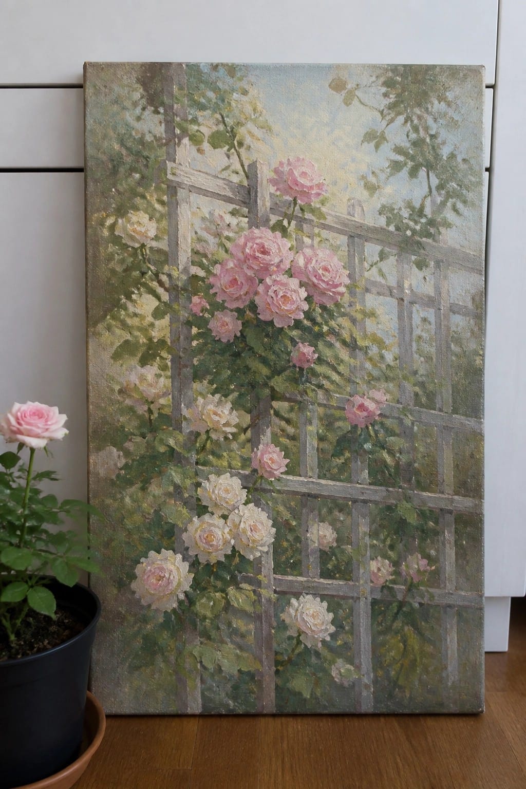 Painting of pink roses on trellis beside potted rose plant on floor
