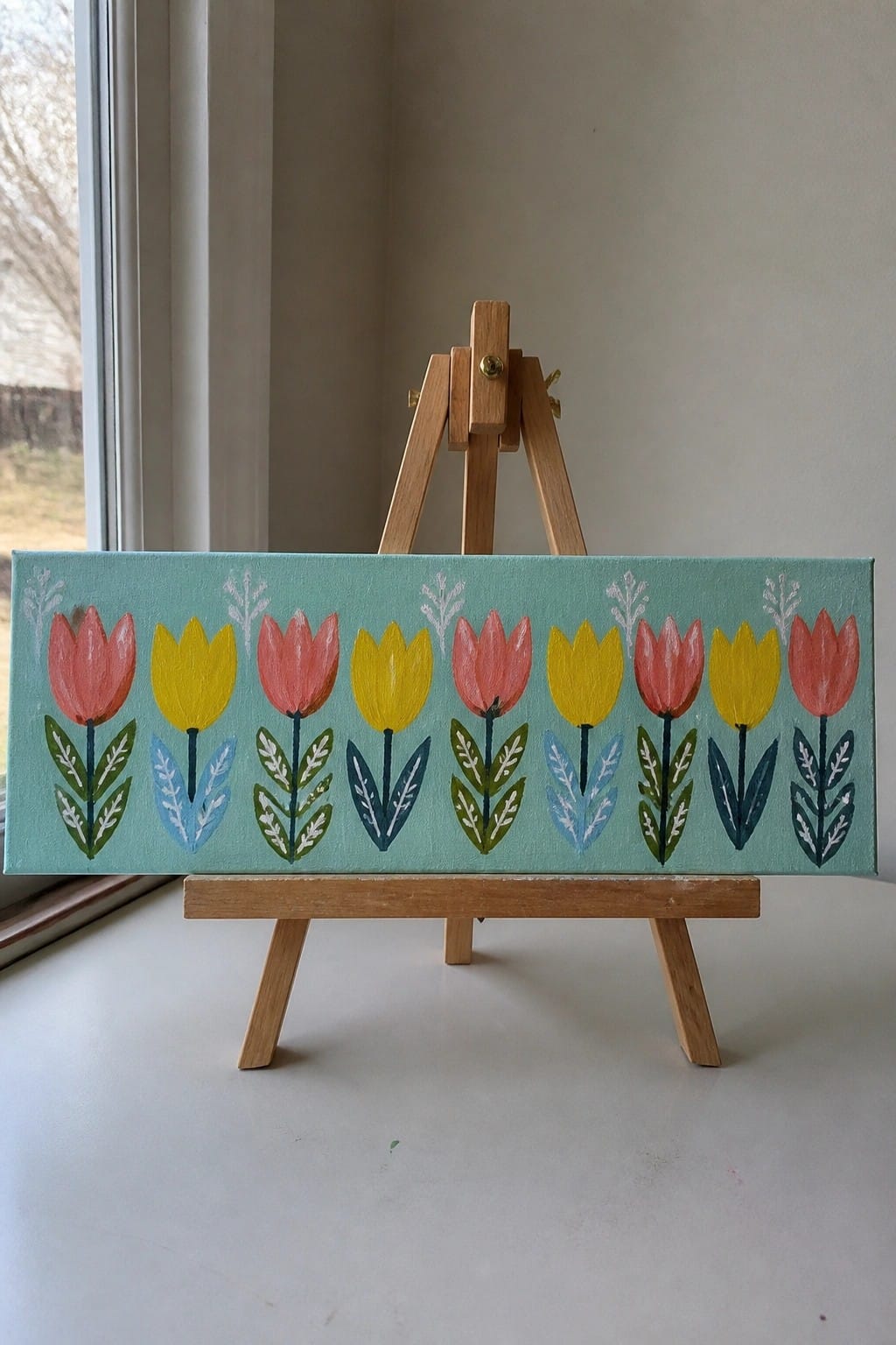 Row of pink and yellow tulips on mint green canvas atop wooden easel