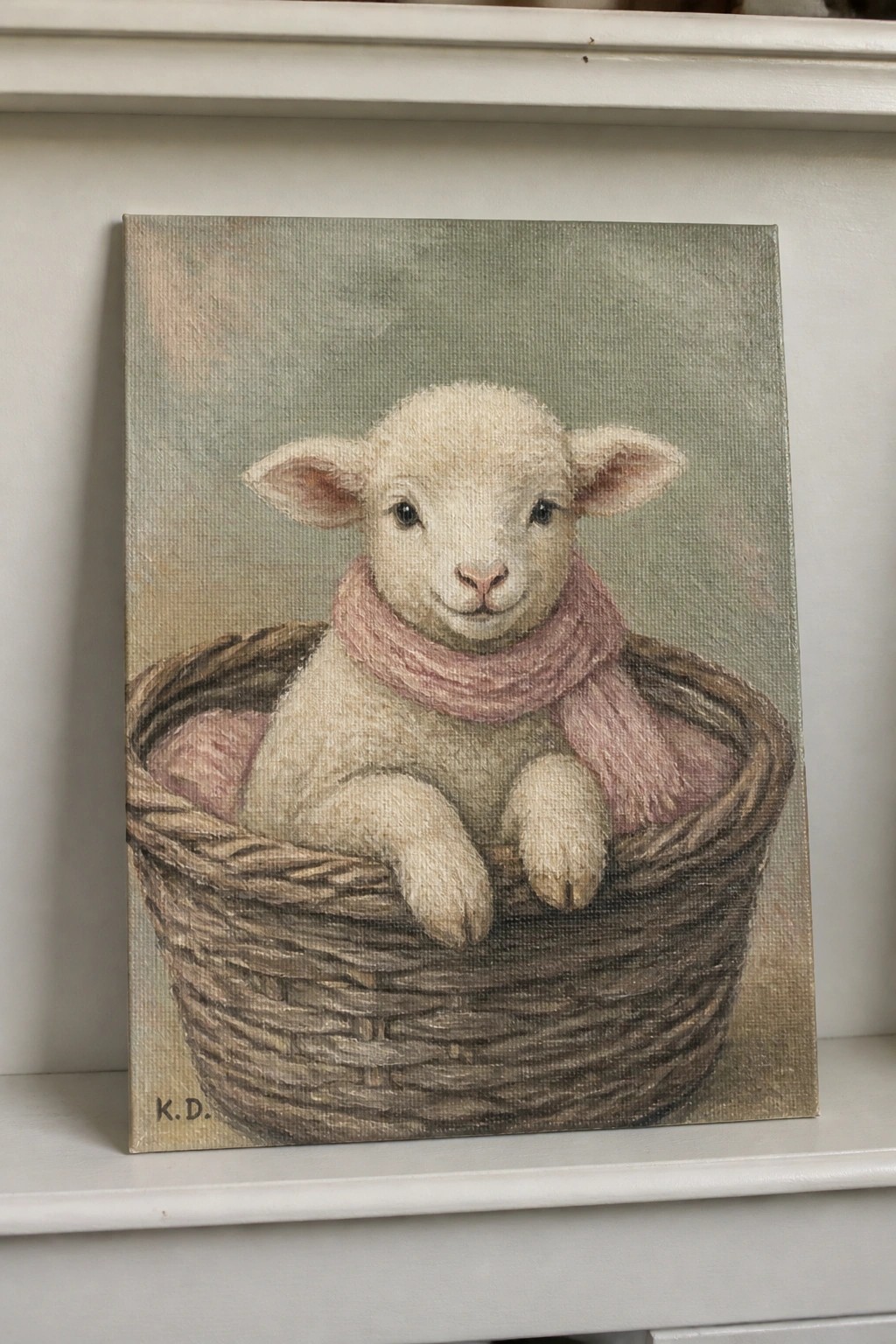 White lamb wearing pink scarf rests in woven basket on soft green canvas