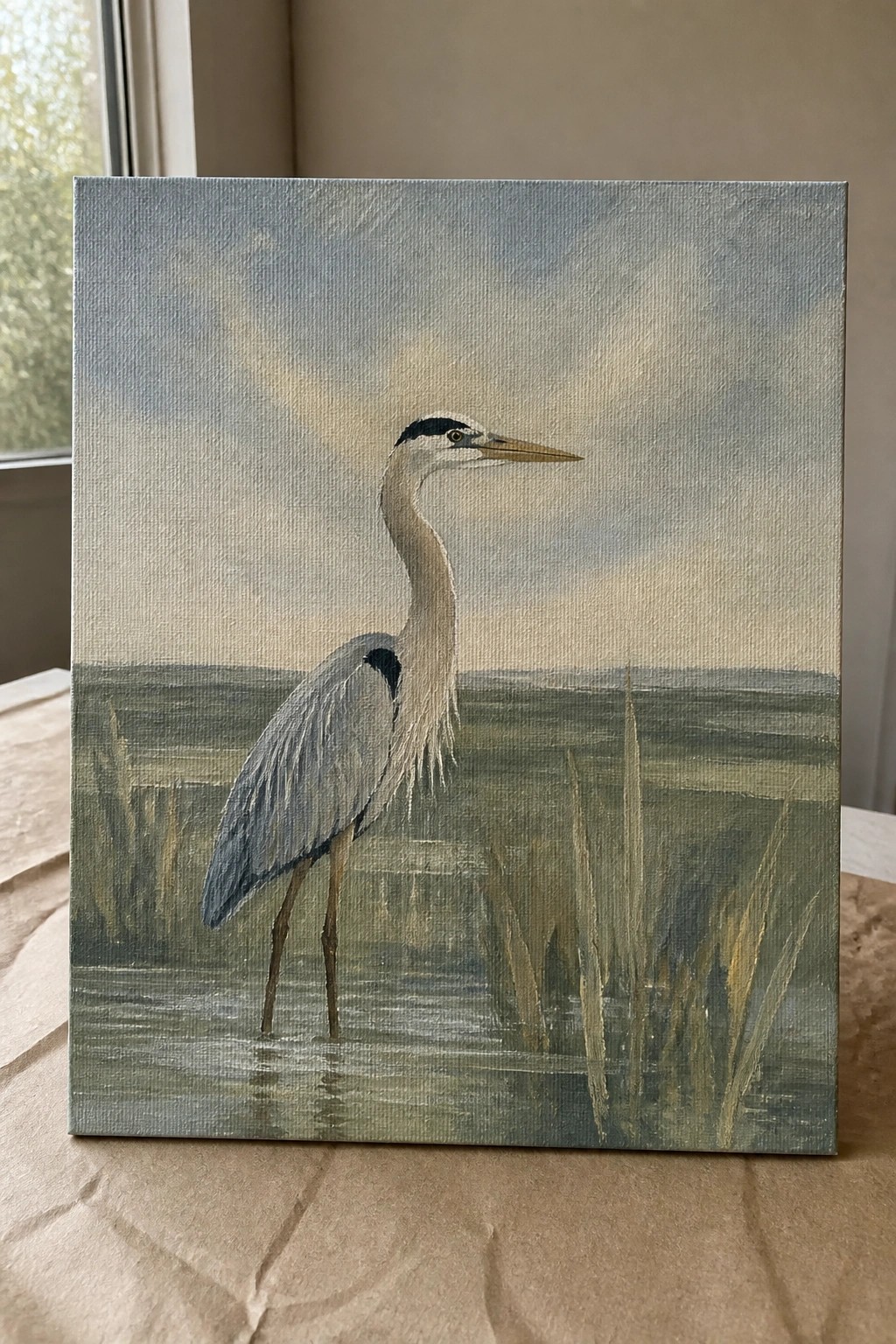 Realistic painting of a tall gray heron standing in shallow marsh water with reeds.