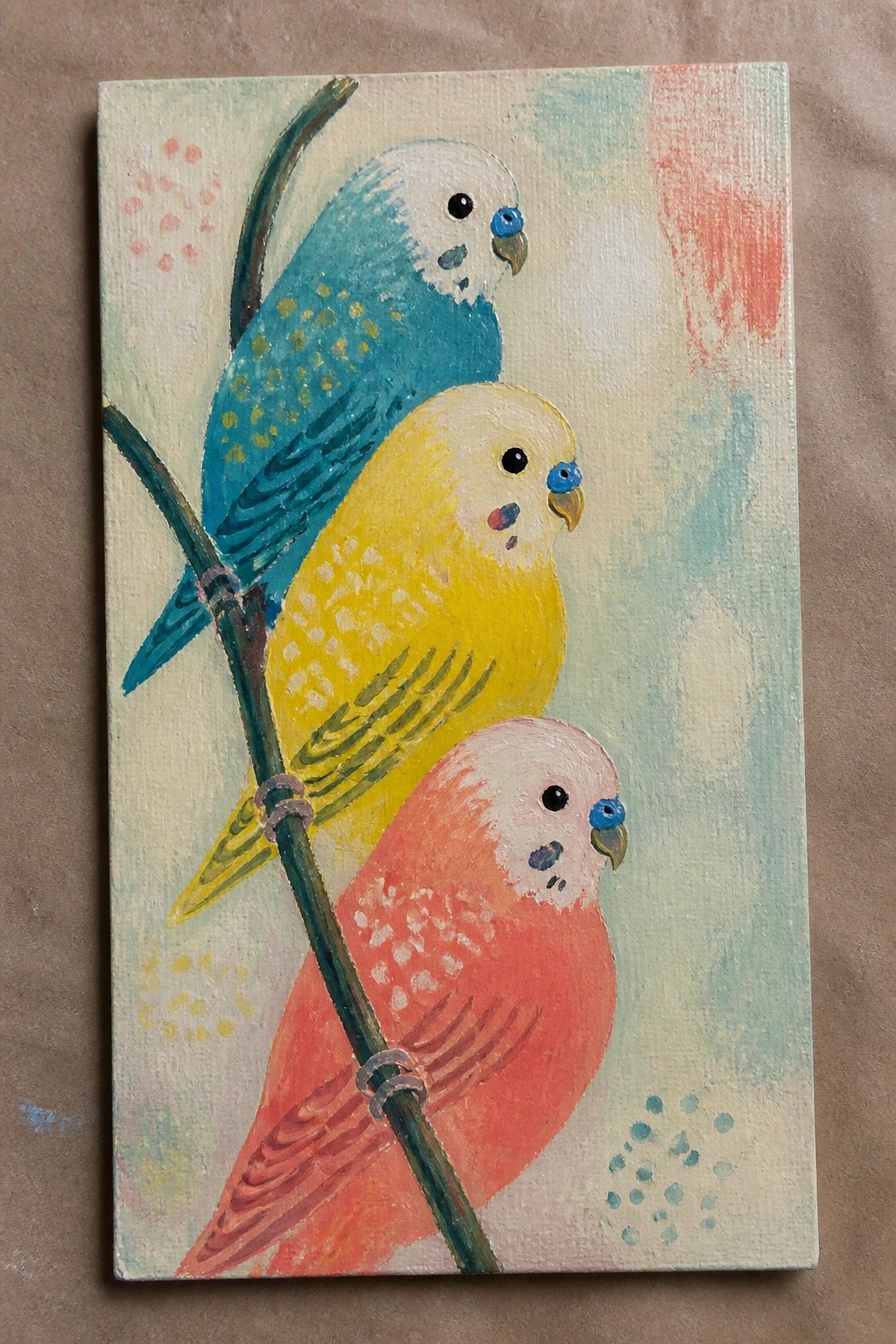 Three colorful budgies in blue, yellow, and pink perched on a branch