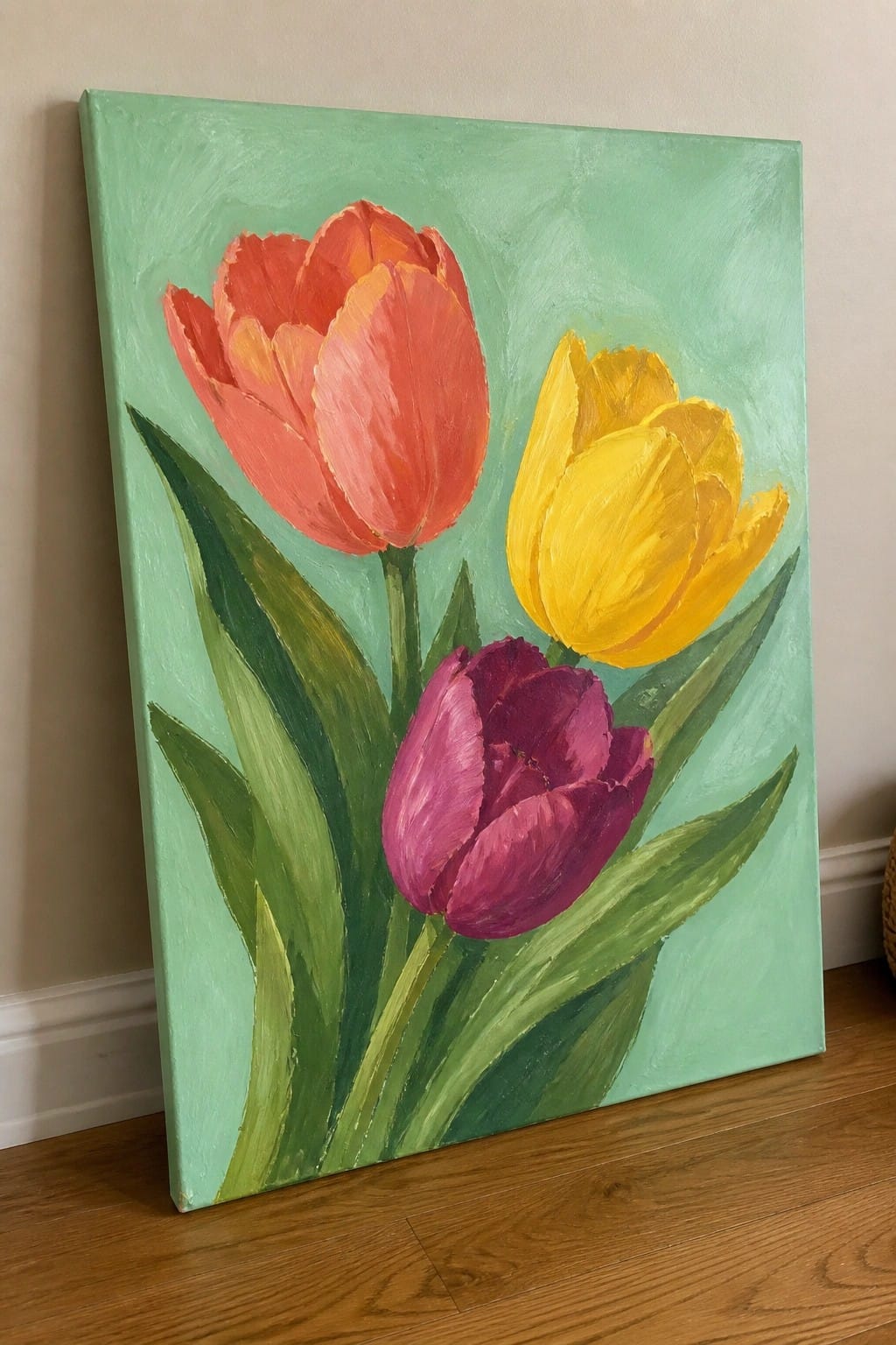 Three colorful tulips in red, yellow, and purple with green leaves on light green canvas.