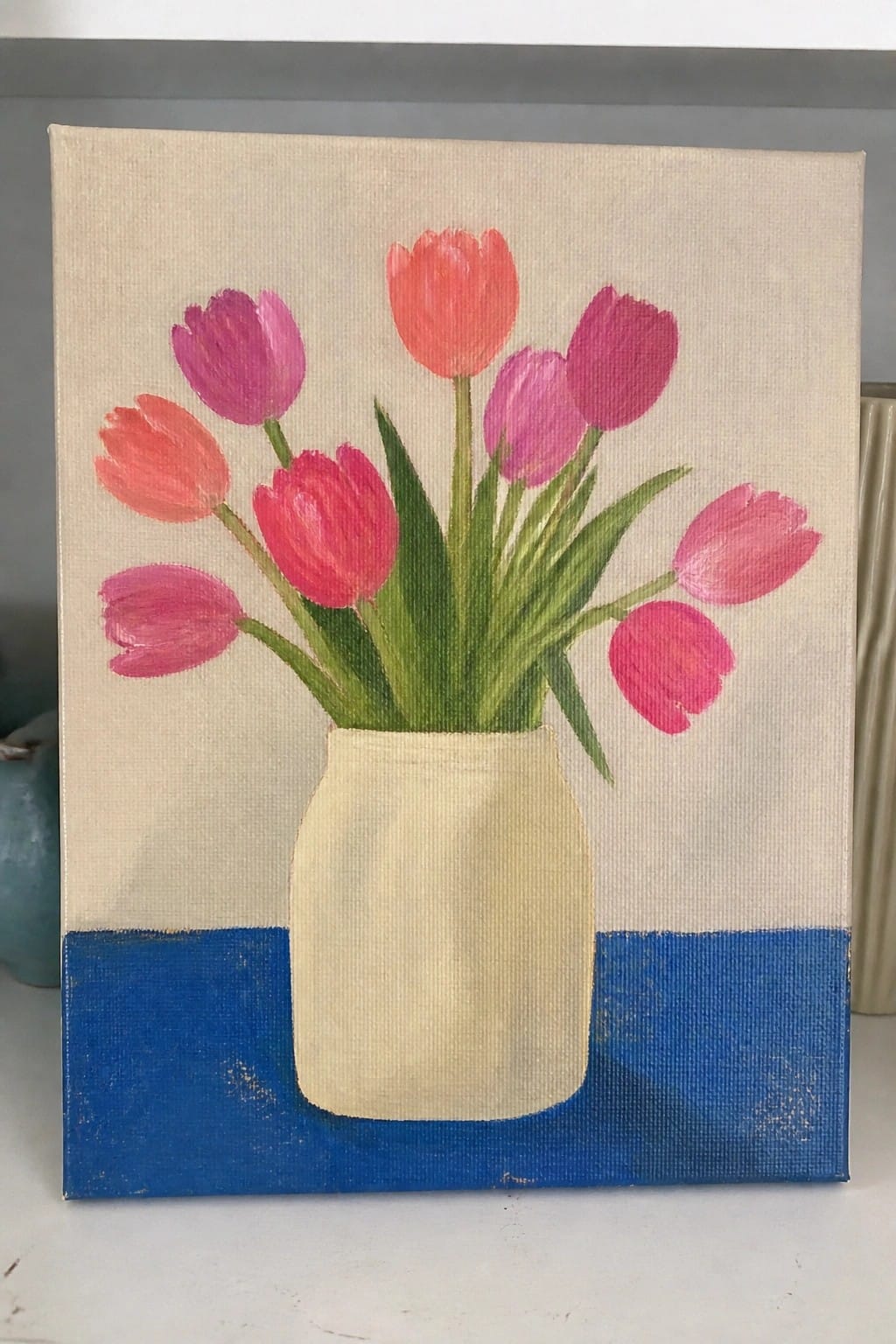 Pink and purple tulips in a white vase on blue surface.