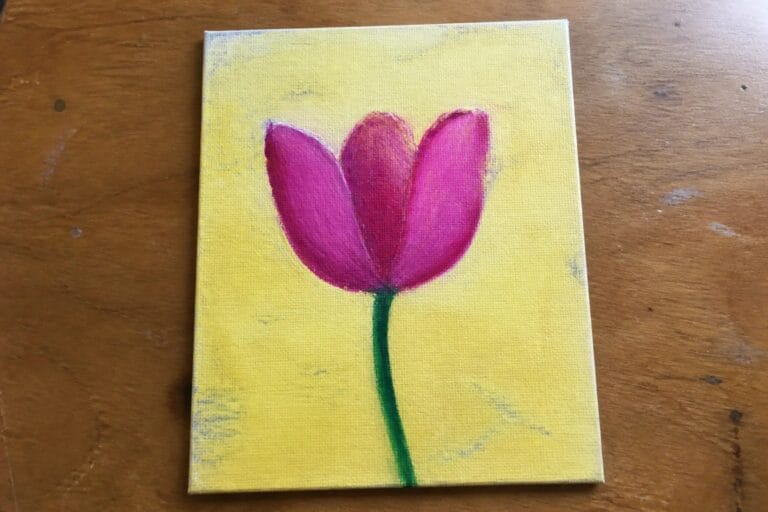 Pink tulip with green stem on yellow canvas atop wooden surface