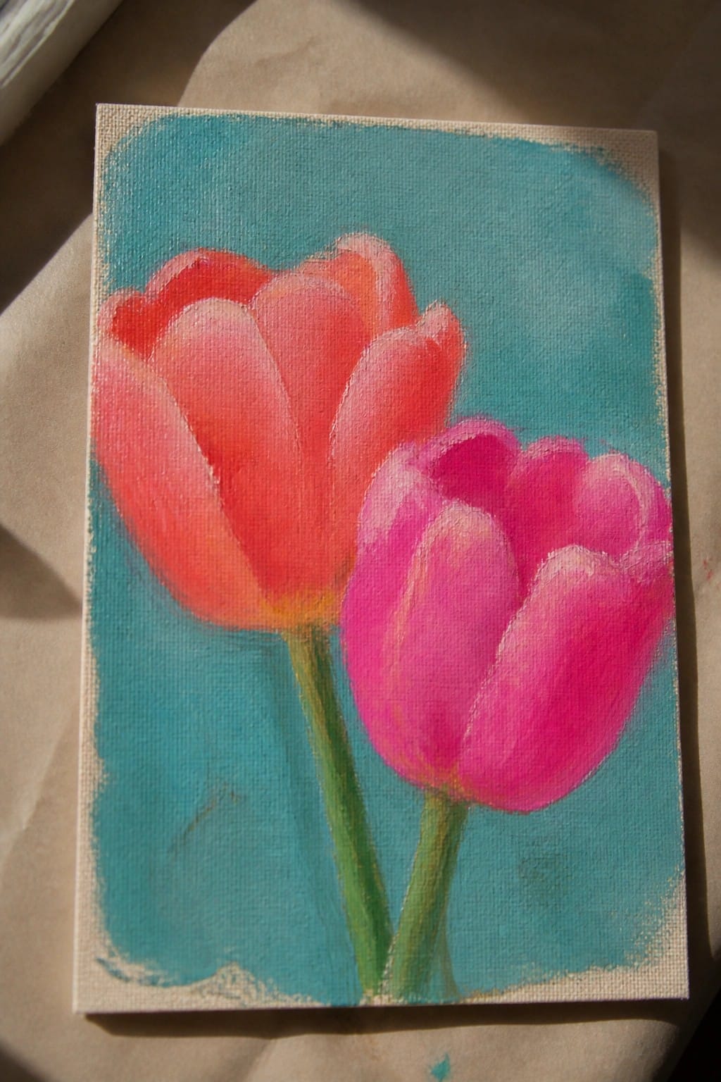 Two vibrant tulips, one orange-red and one pink, on teal canvas background