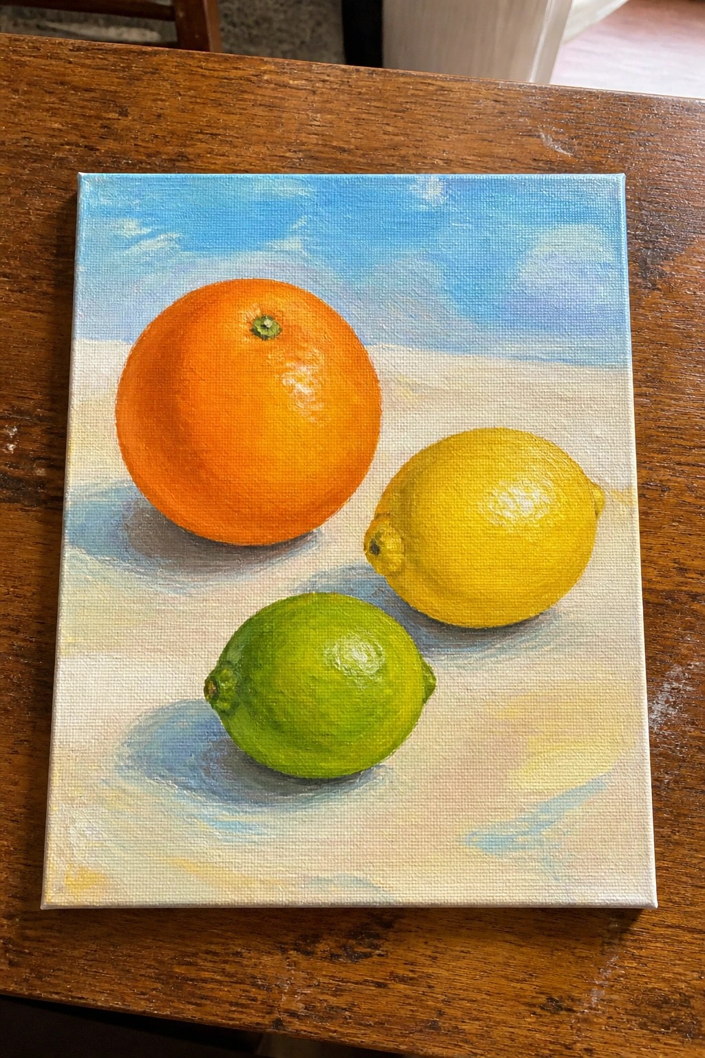 Painting of orange, lemon, and lime on white surface under blue sky