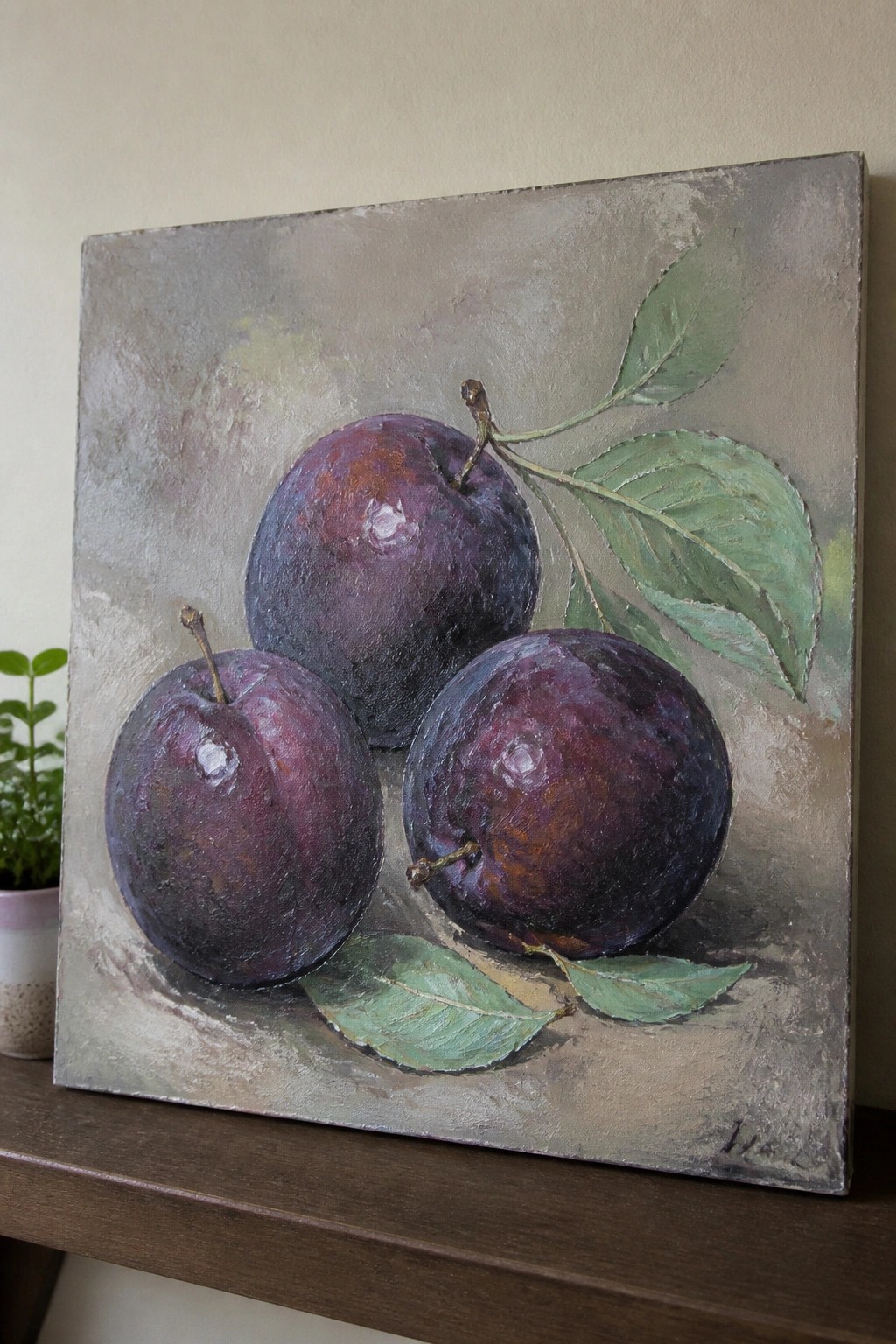 Three dark purple plums with green leaves on textured canvas painting