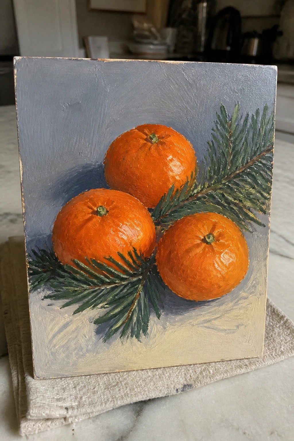 Three vibrant oranges with pine sprigs in an oil still life on blue-gray background.