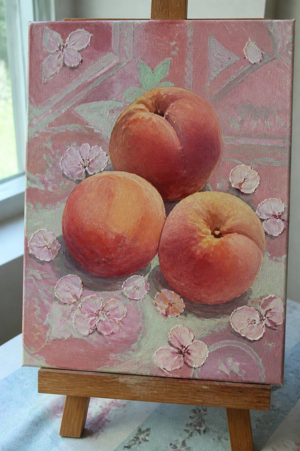 Three peaches on pink floral canvas displayed on wooden easel.