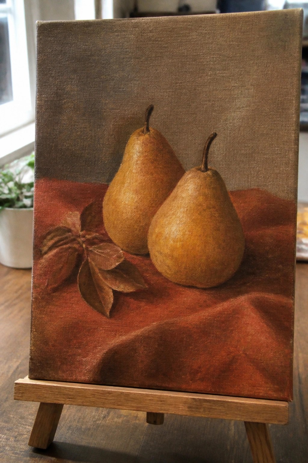 Two pears and leaves on red fabric in still-life painting on wooden easel