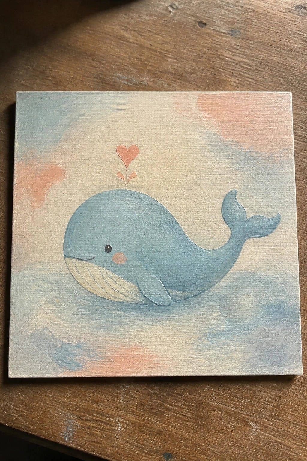 Pastel canvas painting of smiling blue whale with pink heart above on wood