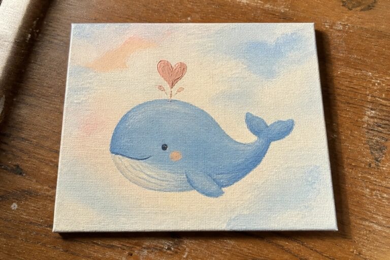 Pastel canvas painting of smiling blue whale with pink heart above on wood