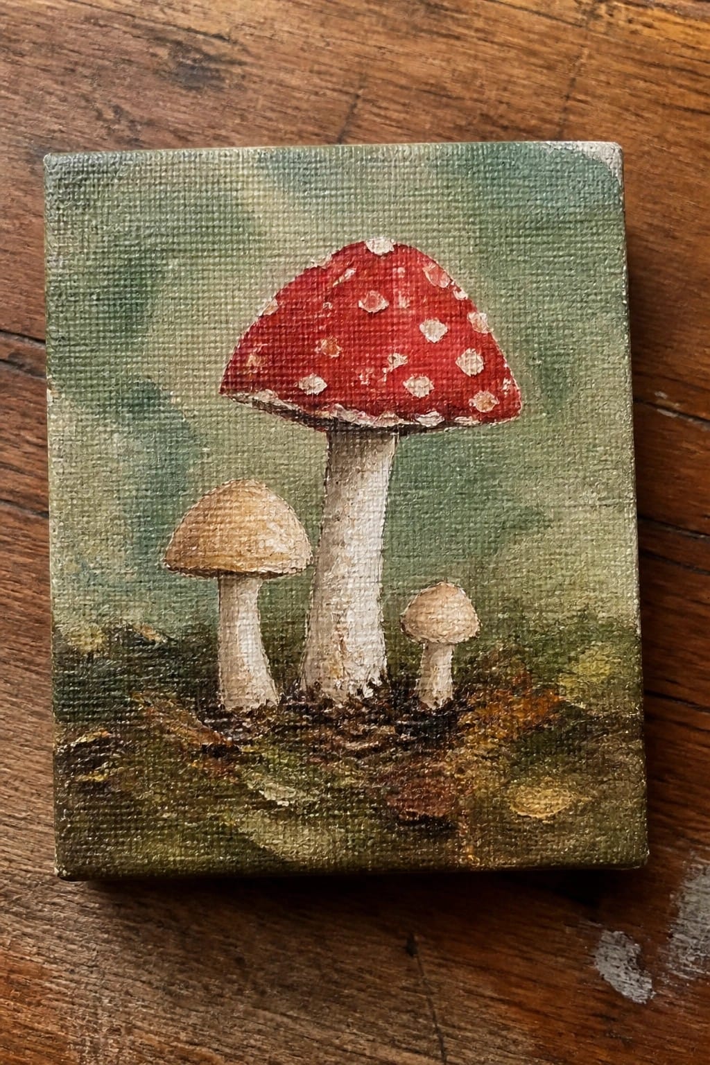 Red spotted mushroom with two smaller brown ones on textured green canvas