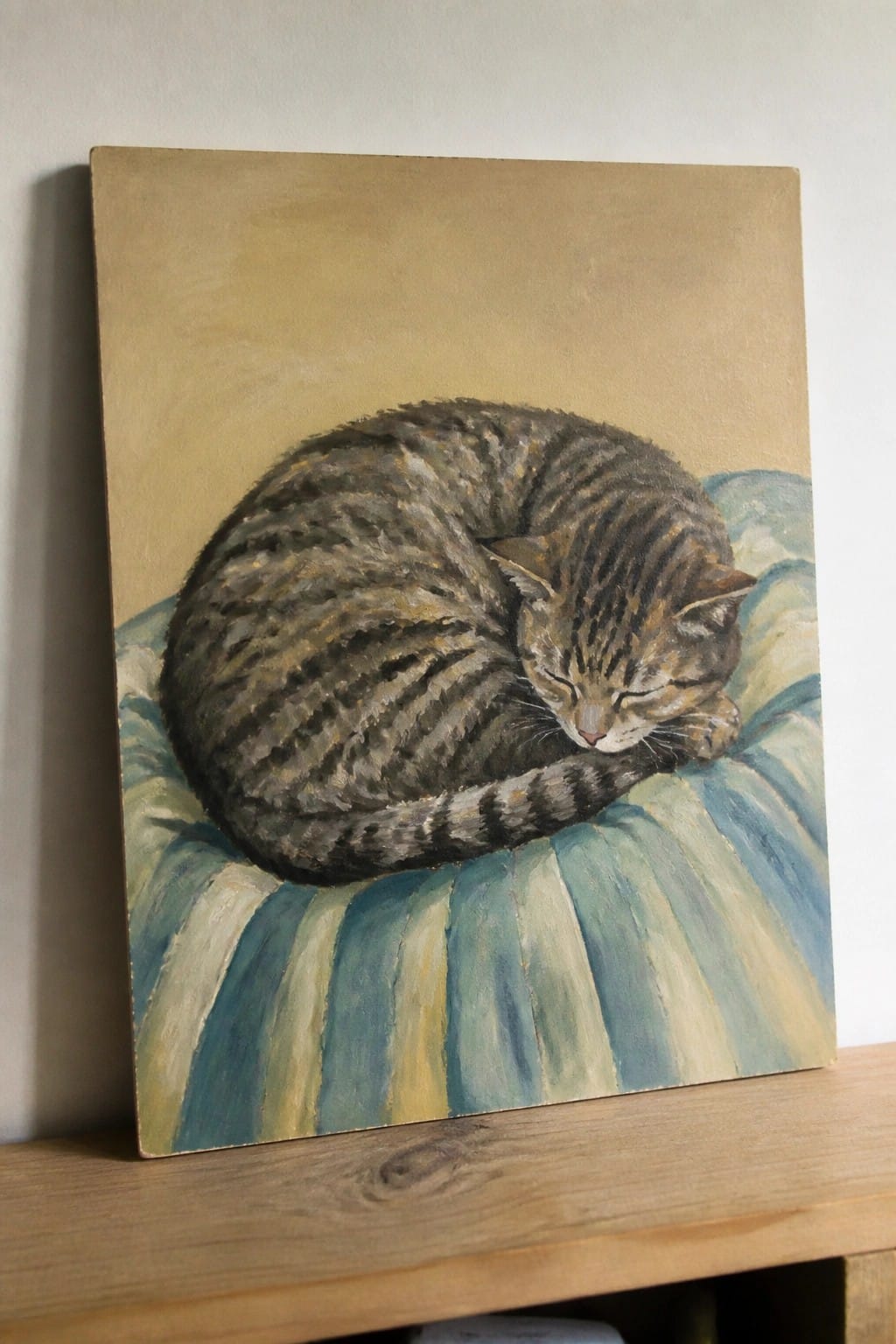Curled tabby cat sleeping on blue and green striped cushion in painting.