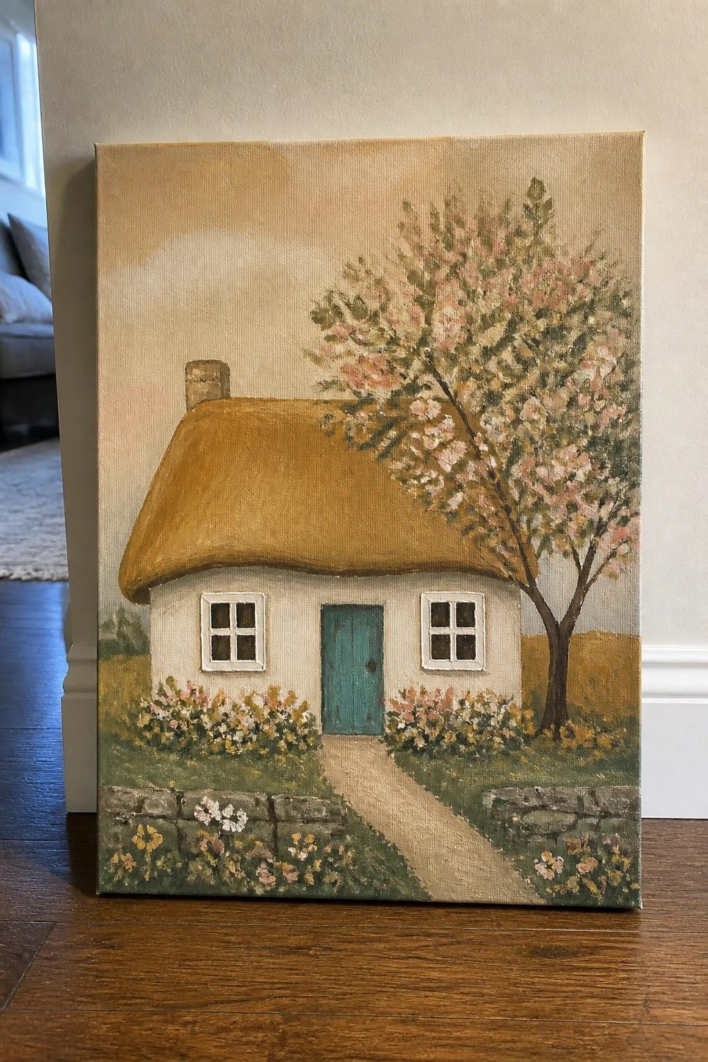 Thatched cottage with teal door, white windows, pink-blossomed tree, flower beds, and stone path