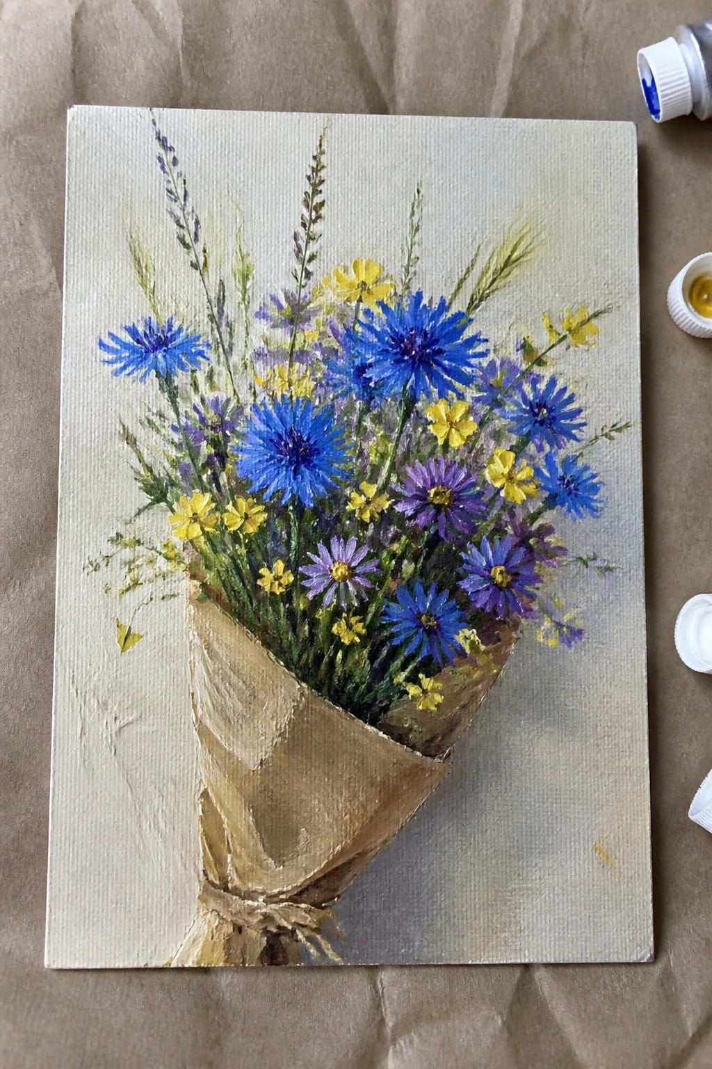 Vibrant bouquet of blue cornflowers, purple asters, and yellow blooms in brown paper wrap