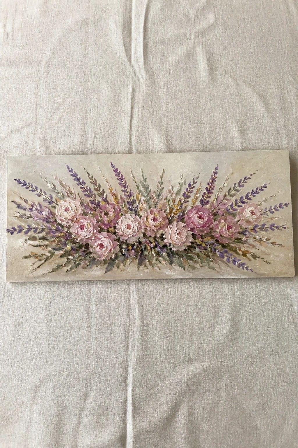 Painting of pink roses with purple lavender sprigs on beige canvas resting on white fabric