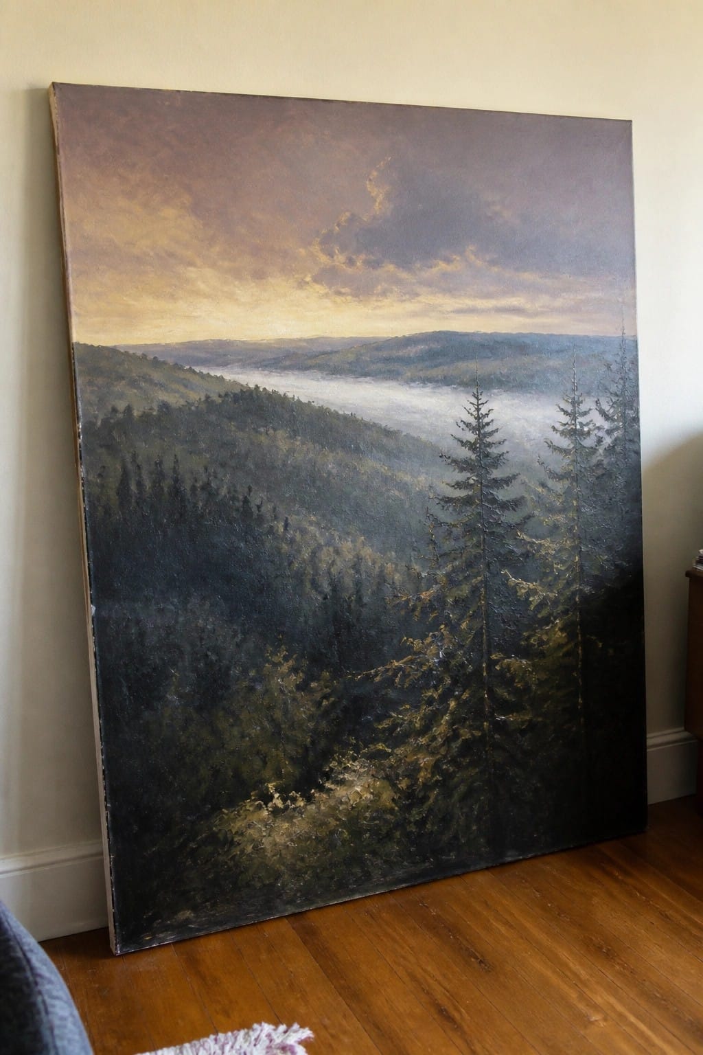 Large landscape painting of misty pine forest at sunset leaning against wall on floor