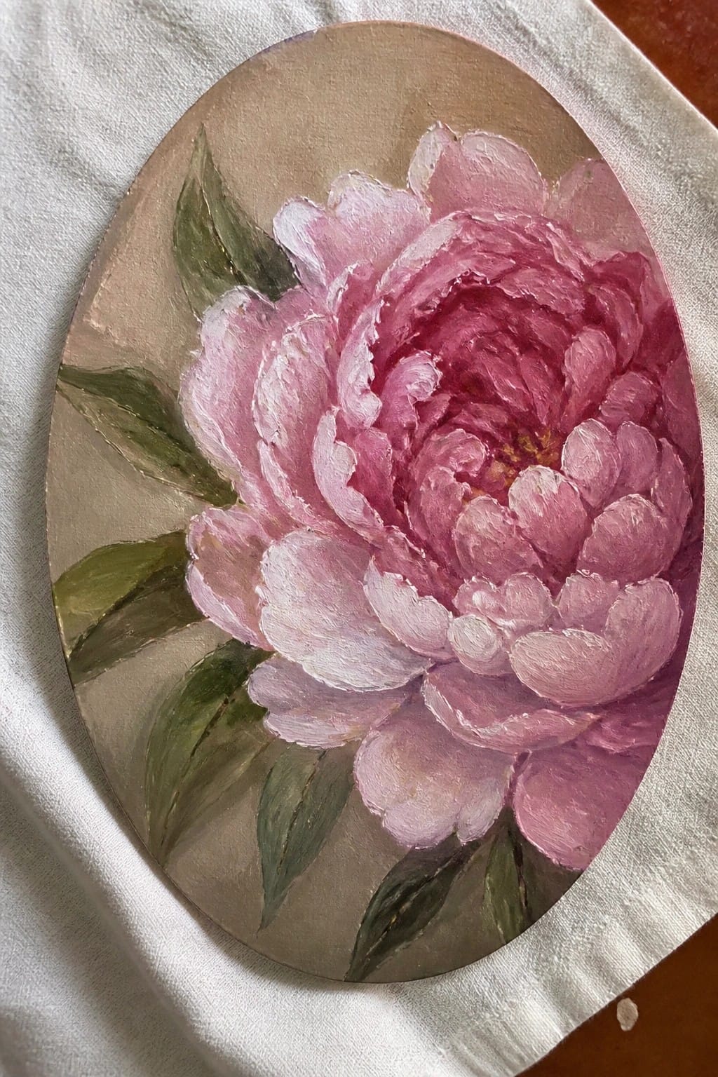 Oval canvas with vibrant pink peony bloom and green leaves on beige background