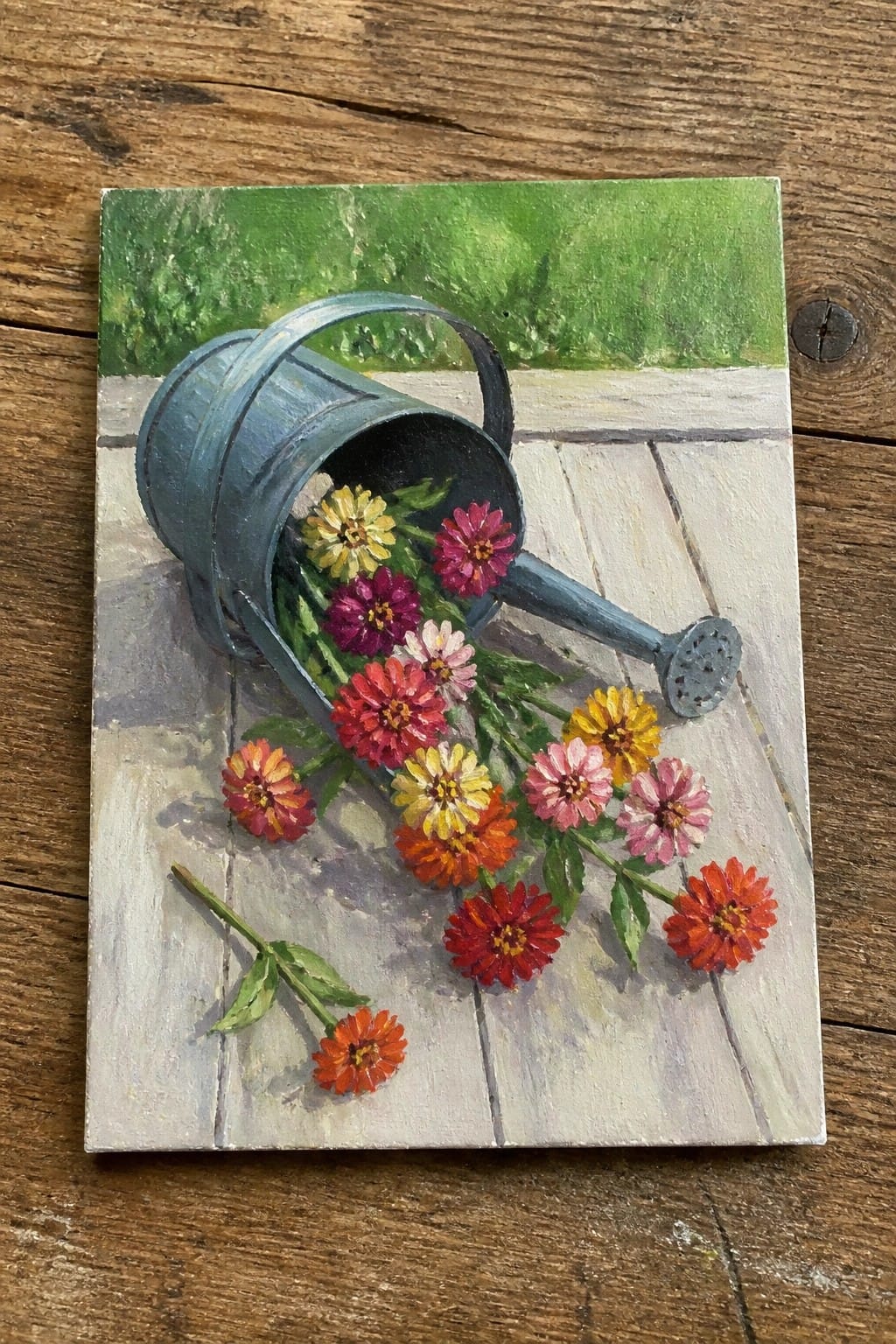 Overturned blue watering can spilling vibrant red, yellow, and pink zinnias on wood.