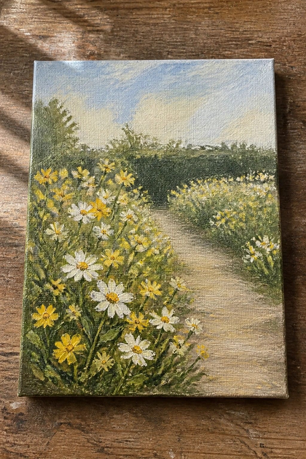 Oil painting of a dirt path lined with white and yellow daisies under a blue sky.