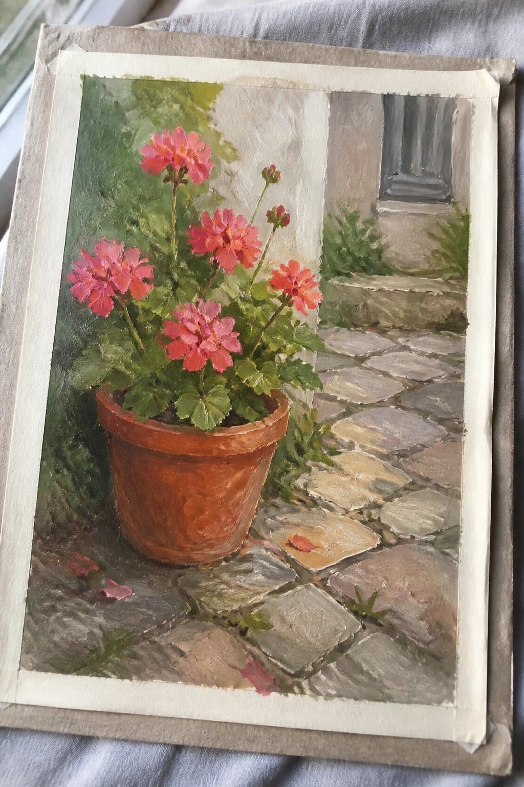 Pink geraniums in terracotta pot on cobblestone path near building entrance