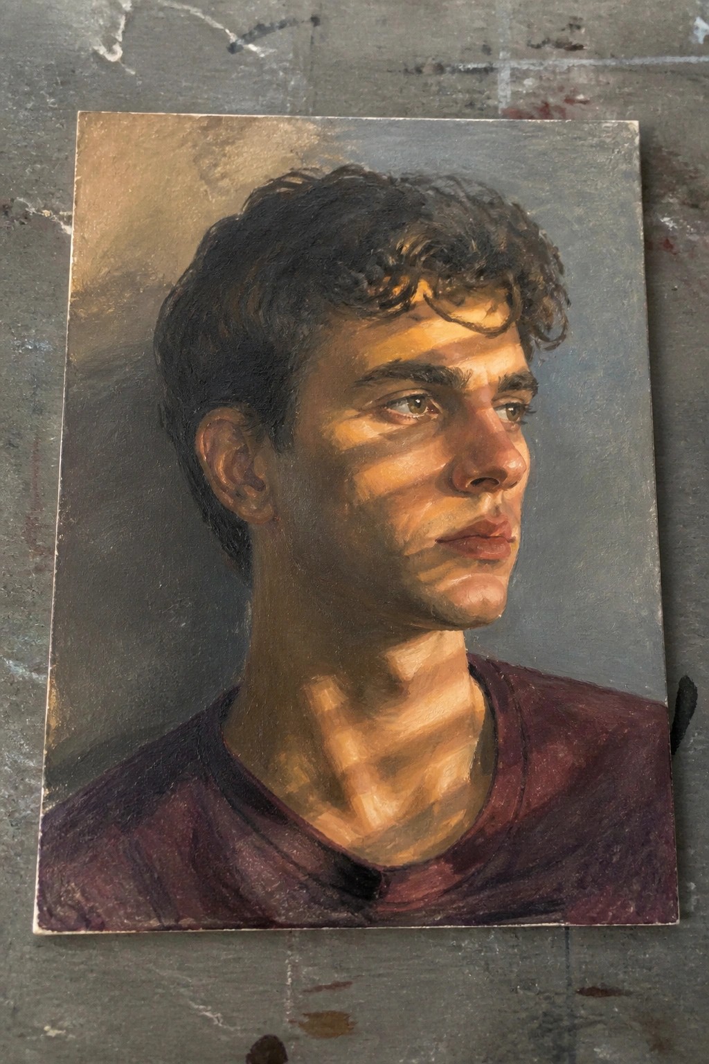 Oil painting of young man with curly hair wearing maroon shirt, dramatic lighting.