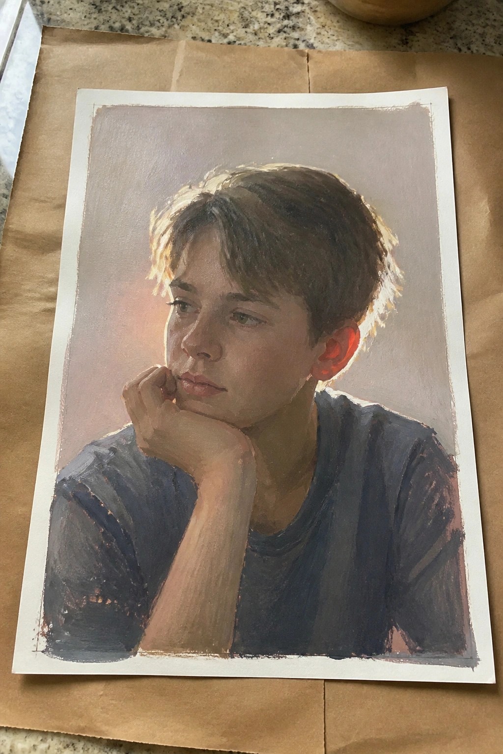 Teenage boy in dark blue shirt rests chin on hand in soft-lit portrait