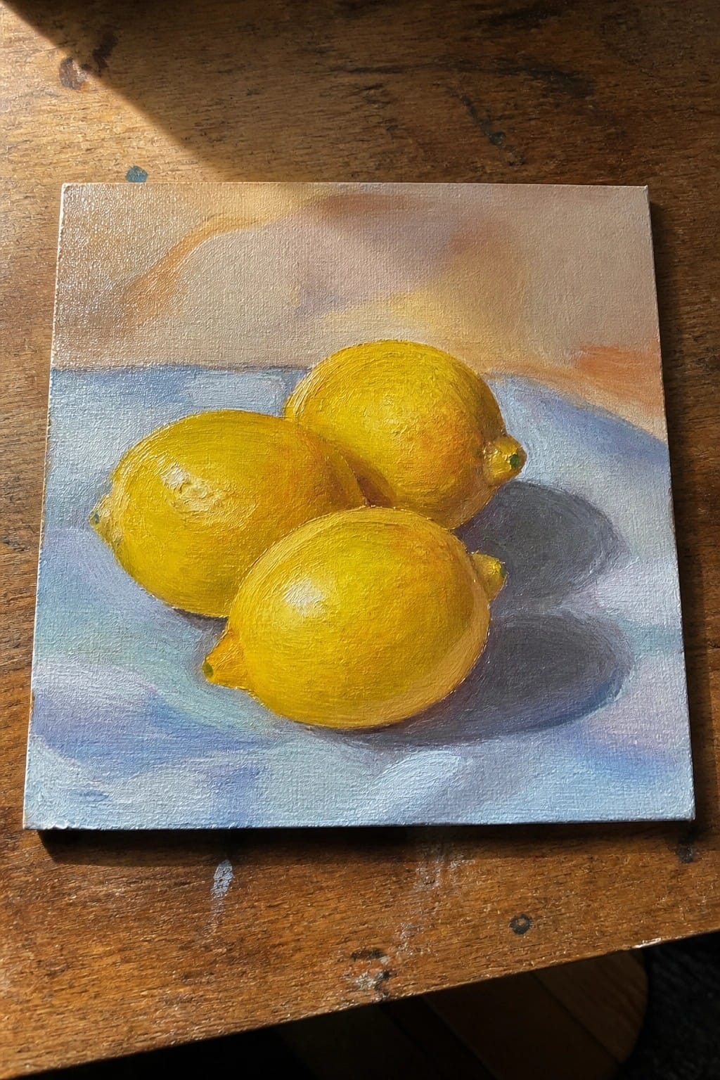 Three yellow lemons on blue fabric with soft shadows in oil painting.