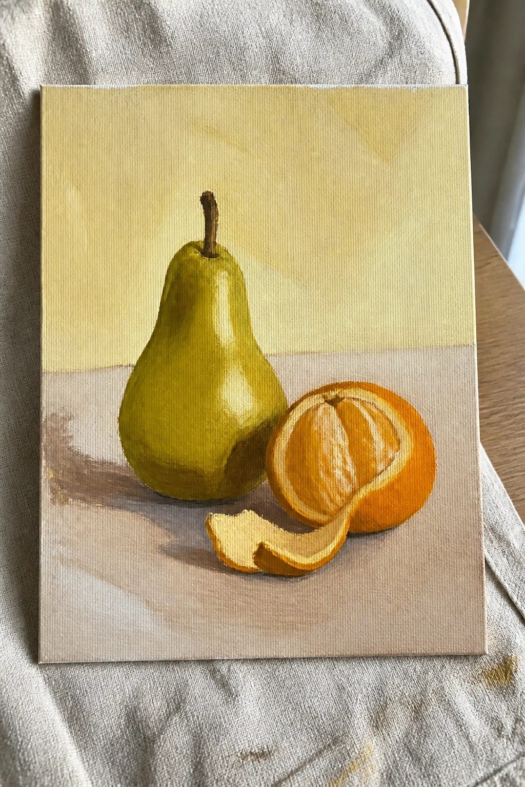 Still life painting of green pear and peeled orange on canvas over white cloth
