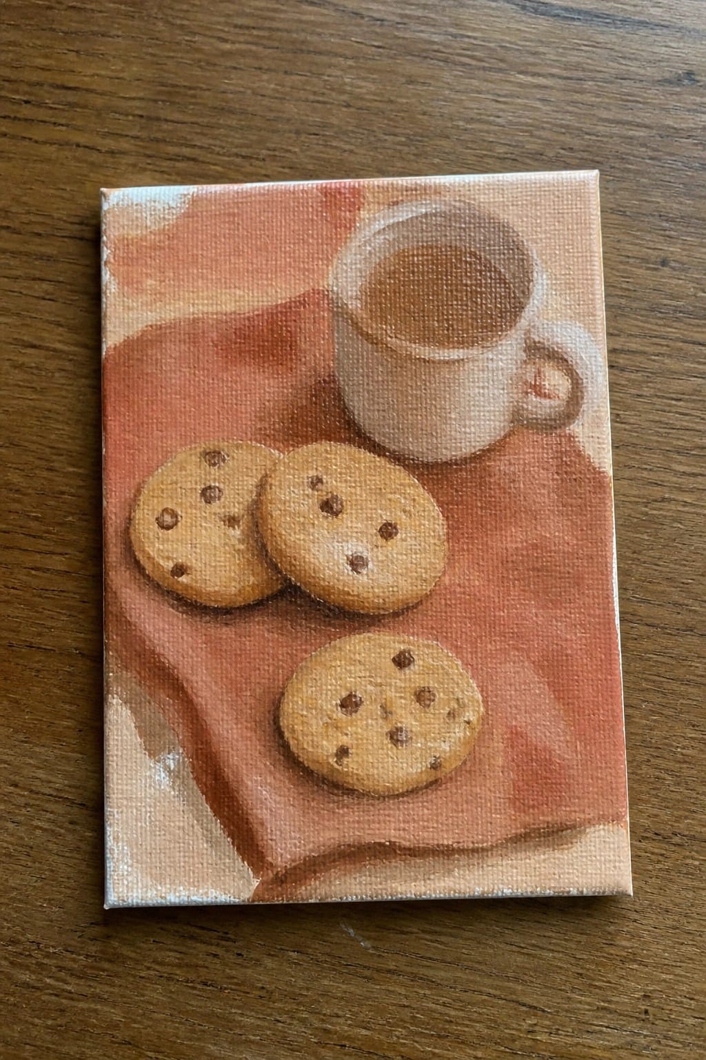 Three chocolate chip cookies beside coffee mug on reddish-orange cloth painting