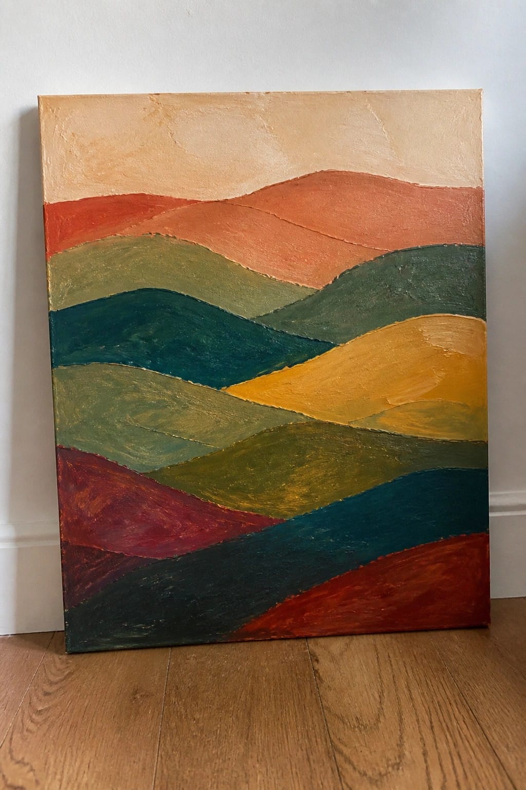 Textured abstract painting of colorful layered hills leaning against a wall on wooden floor.