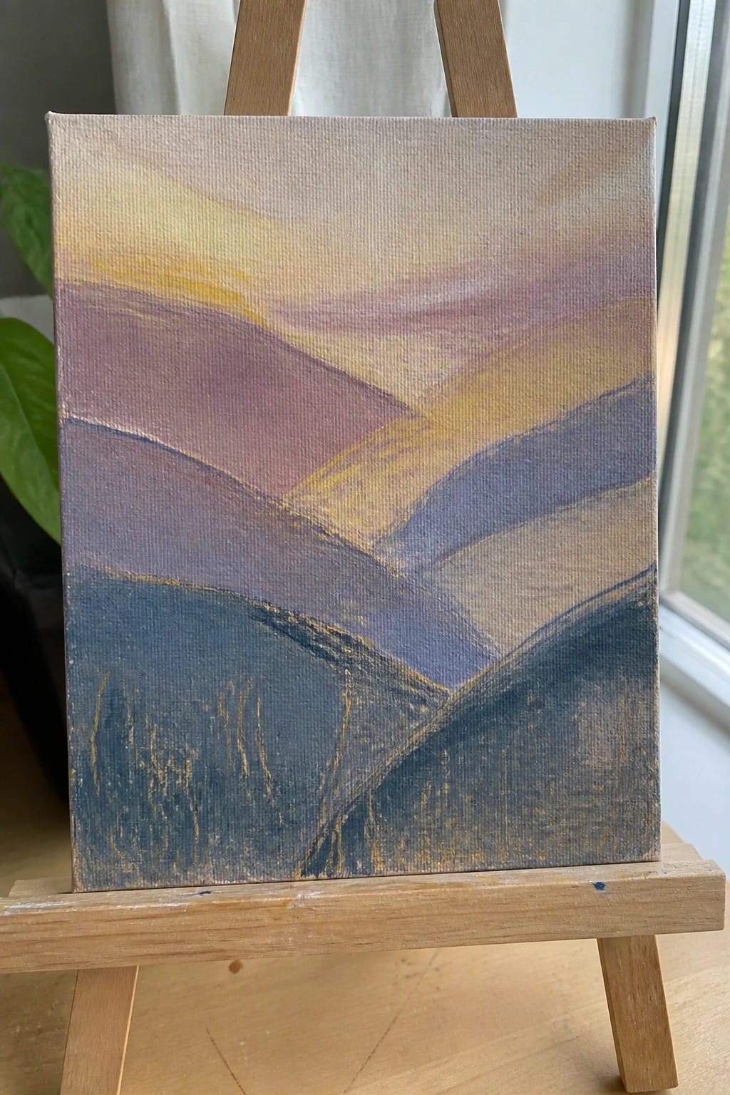 Abstract layered landscape in blues, purples, and yellows on wooden easel.