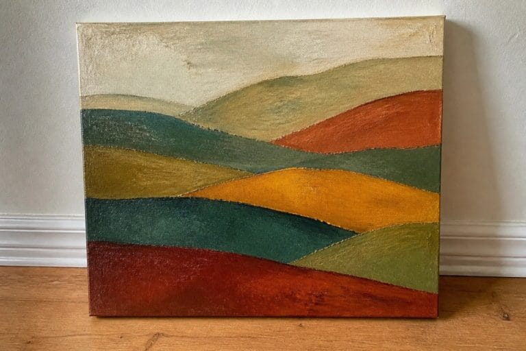 20 Gorgeous Abstract Landscape Oil Painting Ideas Full of Color and Texture Textured abstract painting of colorful layered hills leaning against a wall on wooden floor.