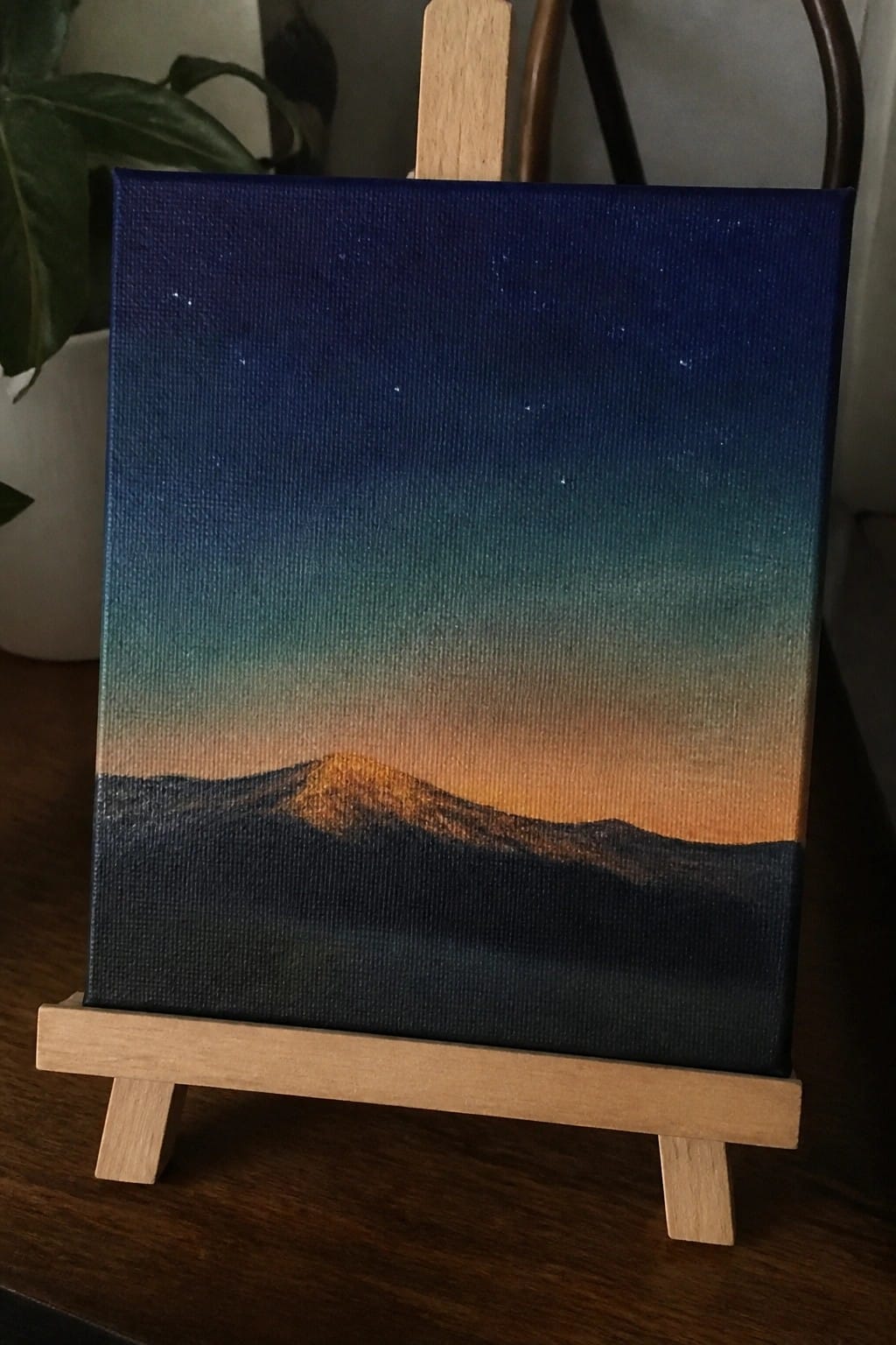 Starry night sky painting with orange mountain glow on wooden easel stand